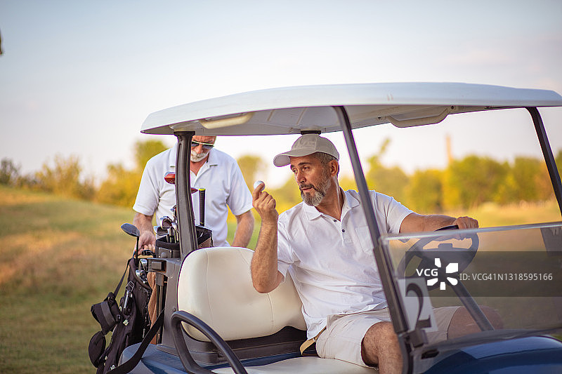 两名资深高尔夫球手在球场上。坐在高尔夫球车上的男人。两名资深高尔夫球手在球场上。图片素材