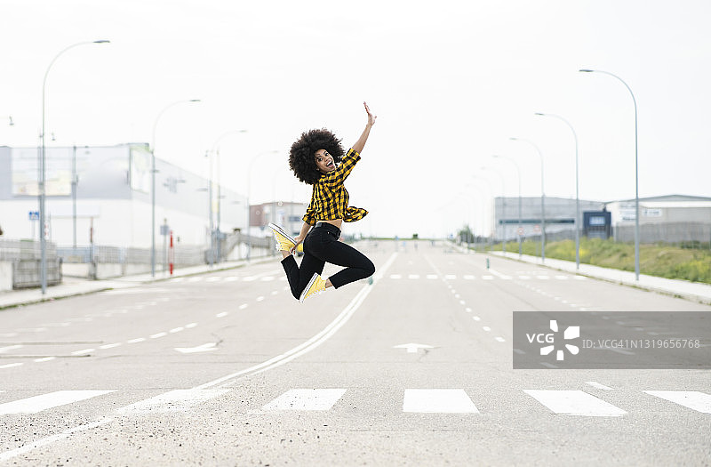 年轻女子高举双臂，在路上跳跃图片素材