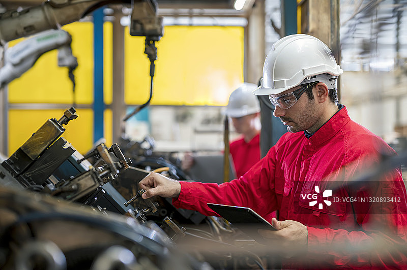 身穿安全工作服的工业工程师在工厂检查或调整汽车零件的机器人焊接装配夹具。他们擅长机器人、焊接控制和提高生产率。图片素材