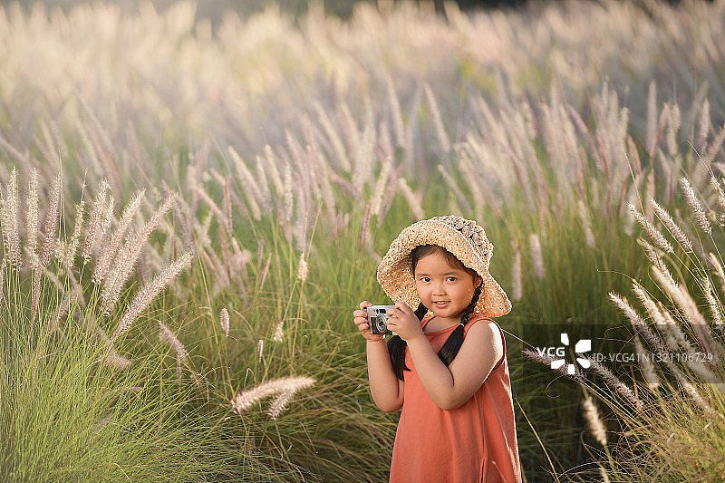 微笑的女孩站在长草中拍照，泰国图片素材