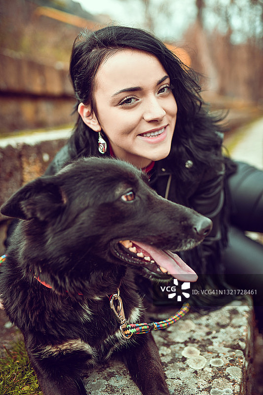 微笑的哥特女性与宠物黑狗在户外放松图片素材