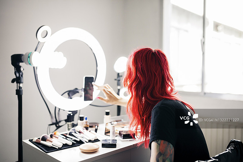 染红头发的女艺术家在工作室用智能手机拍视频图片素材