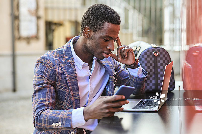 年轻男性企业家在路边的咖啡馆里用手提电脑玩手机图片素材