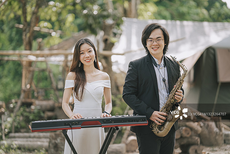 亚洲华人夫妇萨克斯手键盘手乐队表演练习在农村正装图片素材