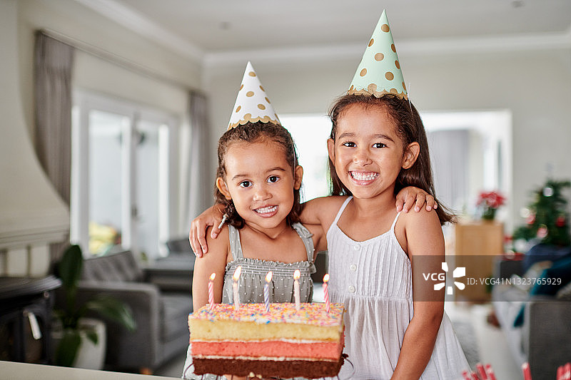 两个可爱的小女孩戴着派对帽，站在一个生日蛋糕后面图片素材