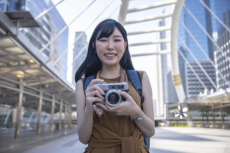 快乐的年轻亚洲女性旅行者与相机看着相机。图片素材