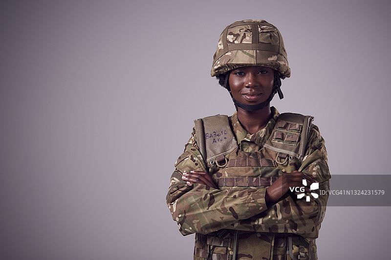 在朴素的背景下微笑的年轻女士兵的工作室肖像图片素材