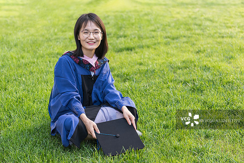美丽的女大学毕业生坐在户外公园的绿草地上图片素材