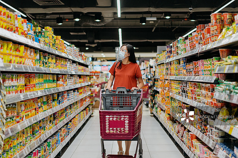 亚洲妇女戴着面罩和面罩在超市买杂货图片素材