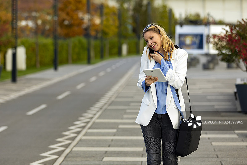 年轻自信的女商人走在城市的街道上，通过手机聊天，制定商业计划。图片素材