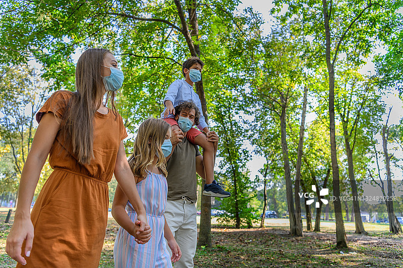 在病毒肆虐期间，幸福家庭和他可爱的孩子们在公园里散步。图片素材