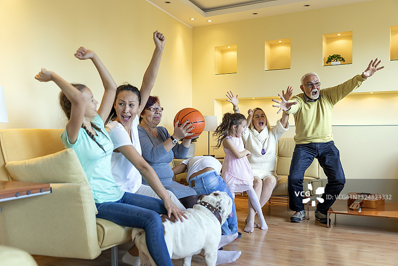 兴奋的多代同堂的家庭正在享受一场篮球比赛在家里。图片素材