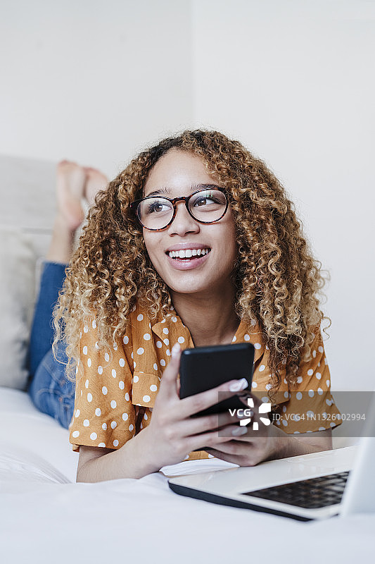 年轻女子用手机看别处，而躺在家里的床上图片素材