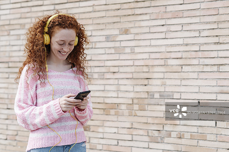 微笑的年轻女子使用智能手机，同时通过耳机听音乐的墙图片素材