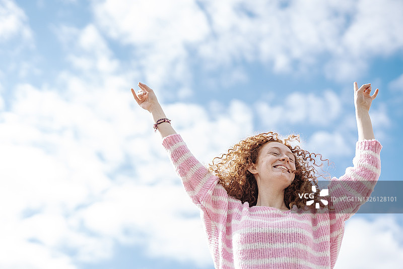 快乐的红发女人举起手臂在天空下跳舞图片素材