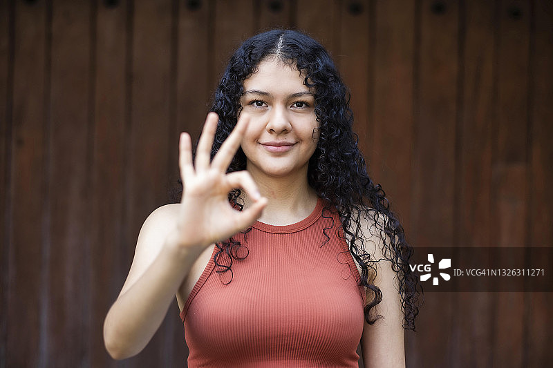年轻的拉丁美洲女性卷头发看着镜头，并给出了OK的手势图片素材