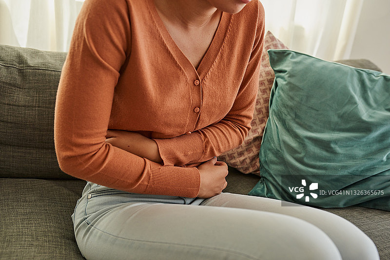 一个女人躺在家里的沙发上，肚子疼图片素材