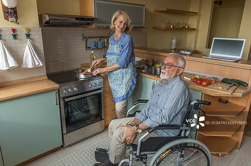 坐在轮椅上的老人和他的妻子享受空闲时间在家做饭。图片素材