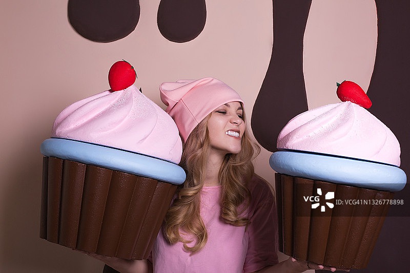 有趣的金发女人戴着粉红色的帽子在工作室享受大蛋糕图片素材