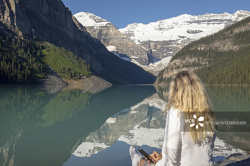 女徒步旅行者放松路易丝湖，反映加拿大落基山脉图片素材