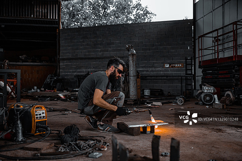 在金属车间的车库，一个金属工人正在使用焊枪在一个金属框架上工作图片素材