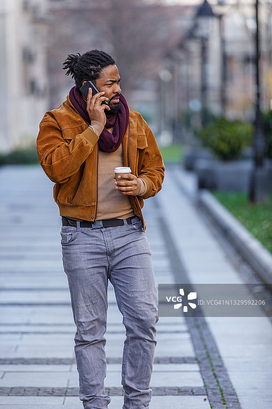 一位非洲青年正走在城市的街道上，喝着咖啡。图片素材