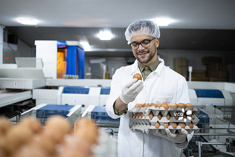 食品加工厂的工人戴着发网和卫生手套，用工业运输和包装机器检查鸡蛋的质量。图片素材