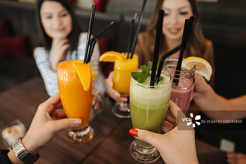 一群年轻的女性朋友坐在咖啡桌旁，喝着不含酒精的鸡尾酒敬酒图片素材