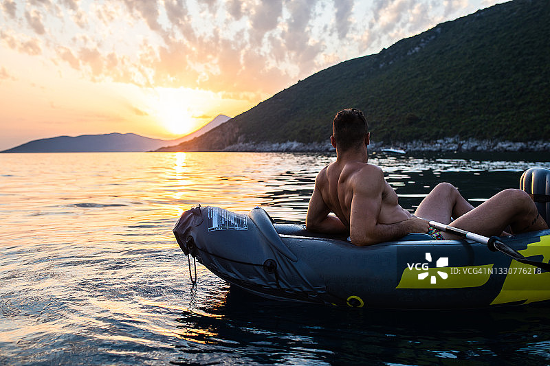 一个坐在皮艇上享受海上日落的年轻人图片素材