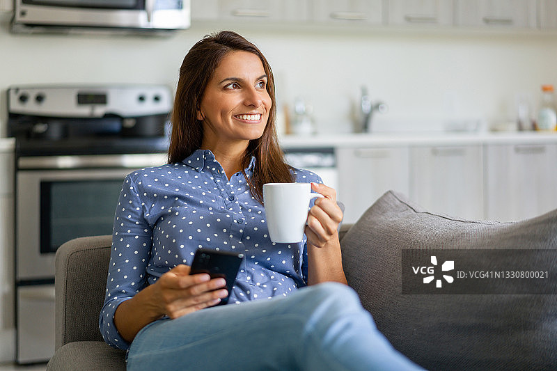 快乐的女人在家边喝咖啡边看手机图片素材