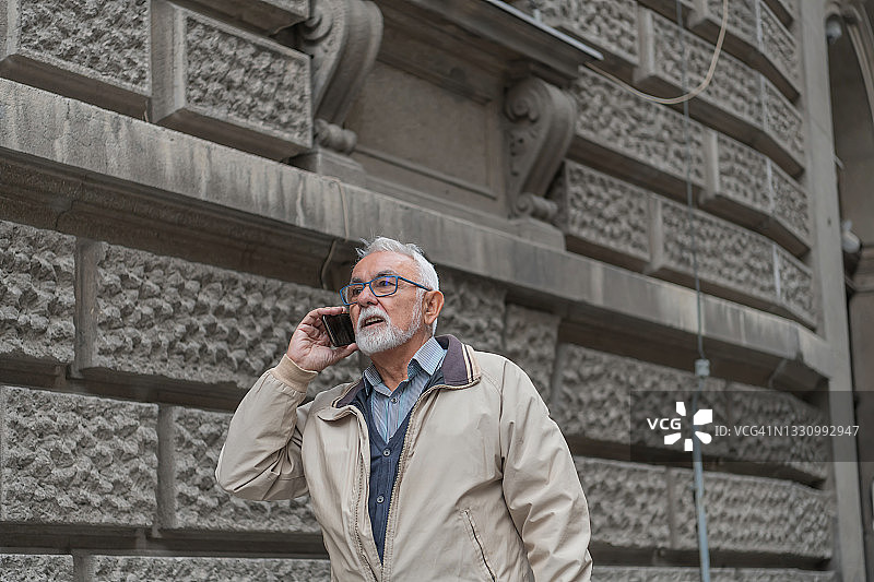 一个上了年纪的男人正在城市的街道上用他的智能手机进行严肃的谈话。图片素材