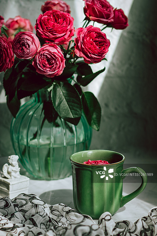 一束粉红色的玫瑰放在一个透明的玻璃花瓶里，旁边是一个绿色的陶瓷杯子图片素材