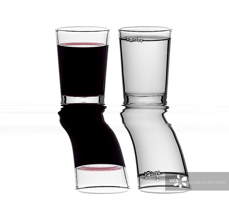 一杯红酒和一杯水在白色背景上，倒映在水面上。图片素材
