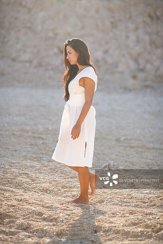 穿着白色夏装的美丽女子独自赤脚行走在石头沙漠图片素材