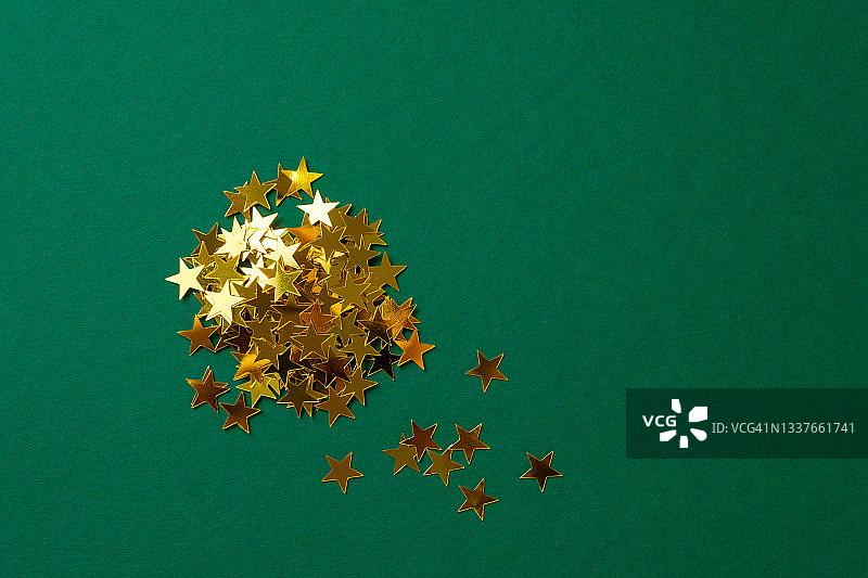 金色和银色的彩纸星星散落在绿色的圣诞节日背景上。复制的空间。图片素材