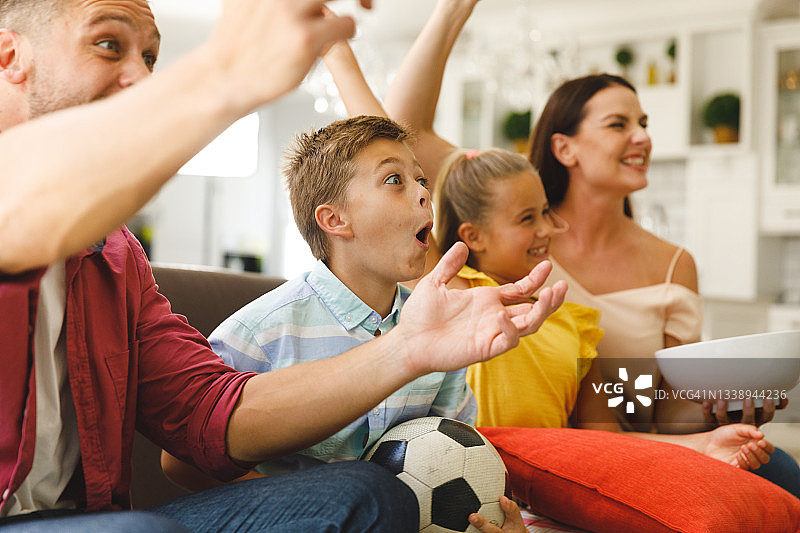 兴奋的白人父母坐在沙发上，女儿和儿子在看电视上的足球比赛并欢呼图片素材