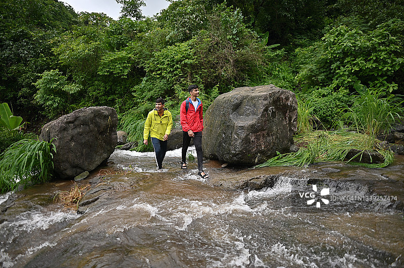 两个年轻人正穿过森林中的一条小溪图片素材