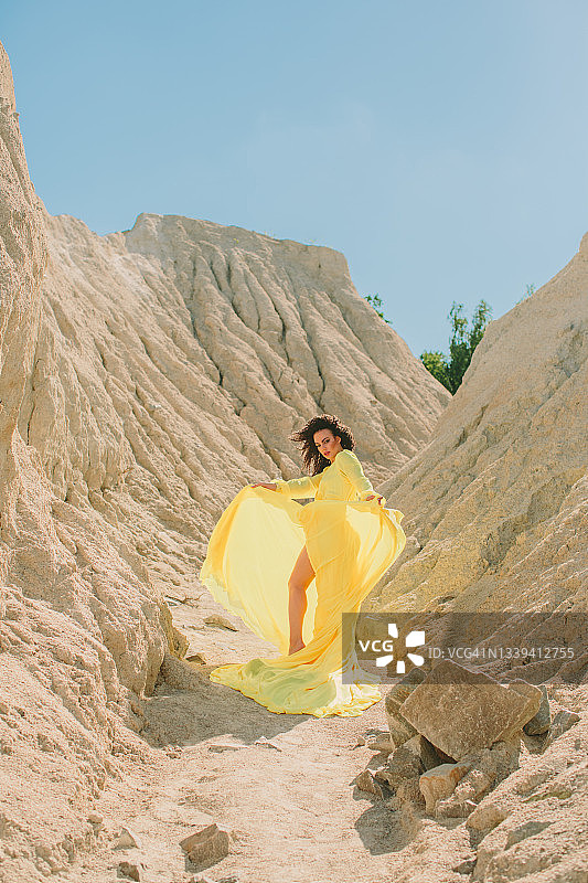 一名年轻女子站在采石场的岸边，靠近沙地，身穿黄色夏装，对着镜头摆姿势图片素材