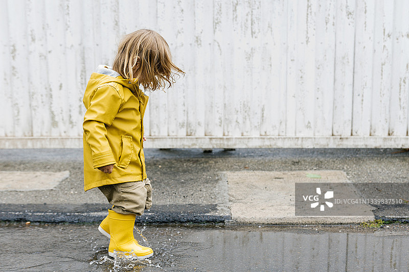 小顽皮的孩子在黄色雨衣和胶靴走在水坑和泼水，而雨后乐趣的侧面视图图片素材