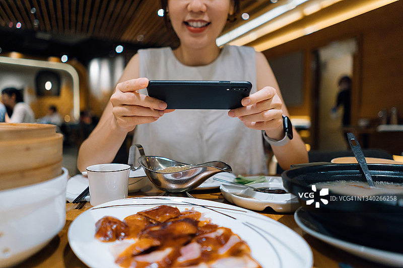 年轻的亚洲女子在餐厅吃北京烤鸭之前，用智能手机拍下了新鲜美味的中国传统美食。外出就餐的生活方式。照相机吃第一文化图片素材