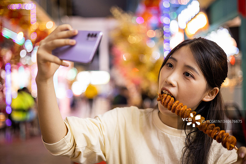 年轻女子在夜市街上用手机自拍图片素材
