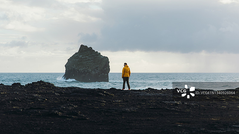 穿着黄色衣服的人凝视着冰岛巨大的岩石和强大的海洋图片素材