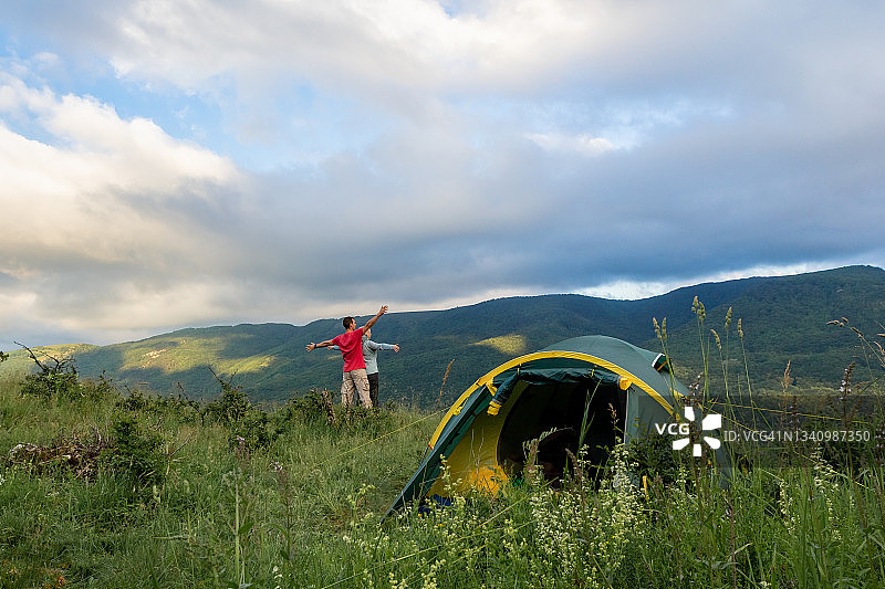 一对年轻的游客在露营帐篷旁边的山顶上欣赏着令人敬畏的夜景图片素材