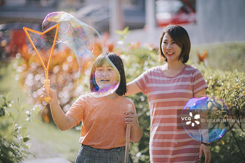 周日早上，亚洲华人妈妈和女儿在后院和猫玩泡泡，在闲暇时间聚在一起图片素材