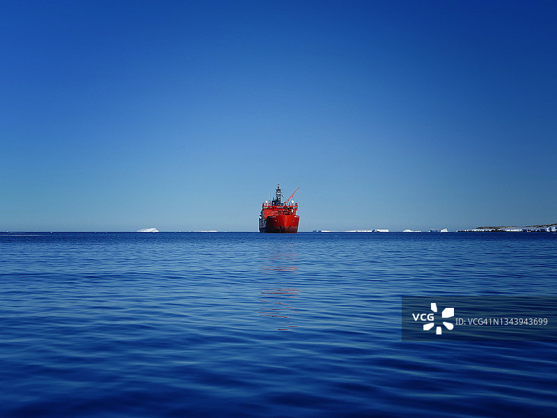 一艘鲜红色的破冰船坐落在南极洲南大洋广阔的蓝色海洋中央。图片素材