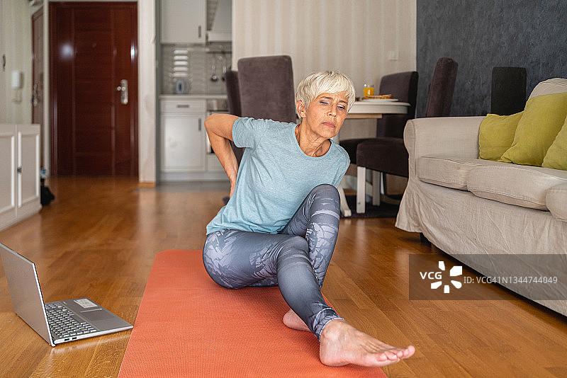 由于背痛，敬业的老年妇女开始了她的家庭锻炼，以减少肌肉疼痛和紧张图片素材