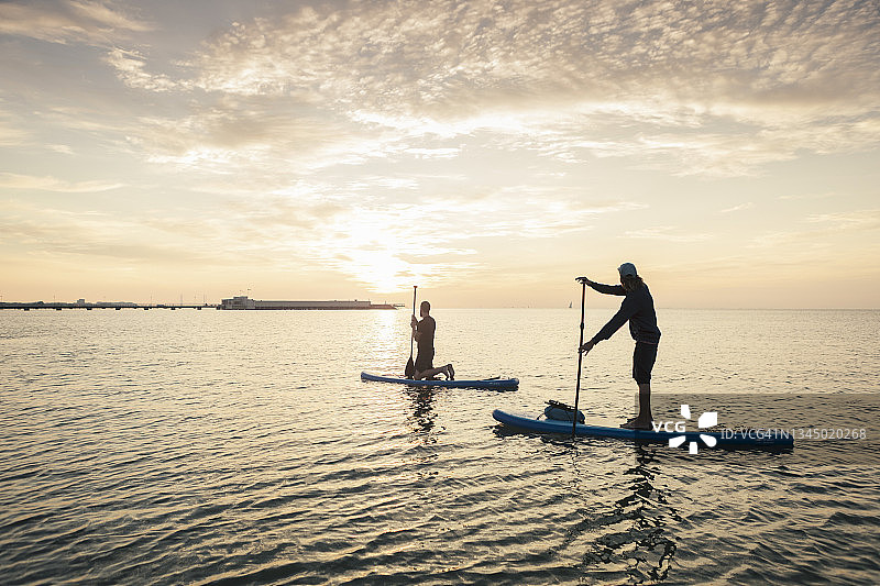 日落时分，男子在海里向男性教练学习划桨图片素材