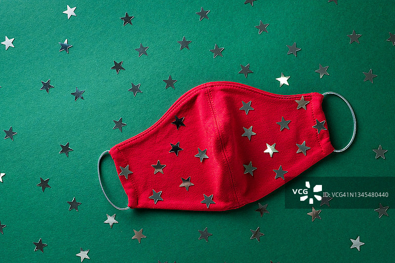 红色医用防护口罩和五颜六色的五彩纸屑在绿色圣诞背景。预防和预防COVID - 19大流行的传播。预防病毒、感染和肺炎。一个快乐健康的圣诞节的概念。图片素材
