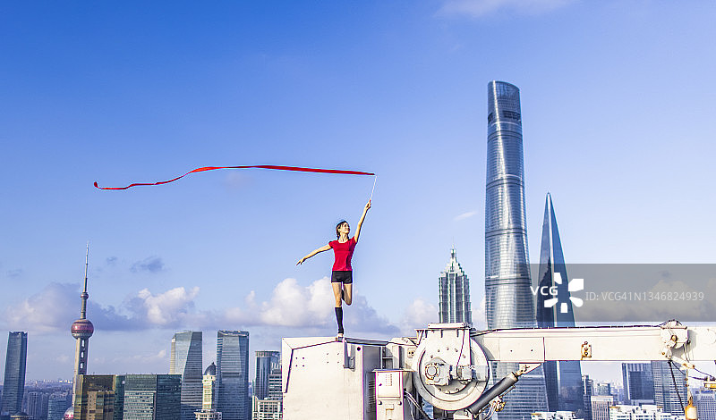 中国上海，一名年轻的女芭蕾舞者在屋顶上用红丝带跳舞图片素材