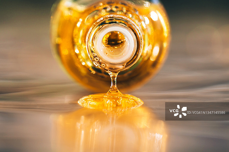 一滴带气泡的亮黄色精油从玻璃瓶中滴下，最终滴在灰色的表面。2021年的流行颜色。极端的特写和正面视图图片素材
